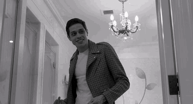 a man in a plaid jacket is smiling in a hallway with a chandelier hanging from the ceiling
