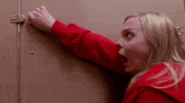 a woman in a red hoodie is pressing a button on a door in a bathroom stall .