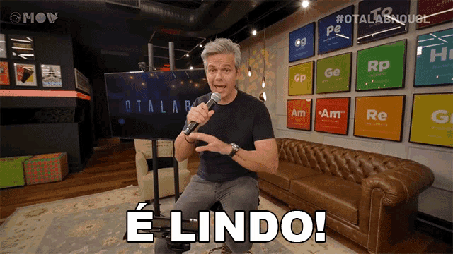 a man holding a microphone in front of a couch and says e lindo