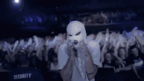 a man in a white mask is singing into a microphone in front of a crowd at a concert .