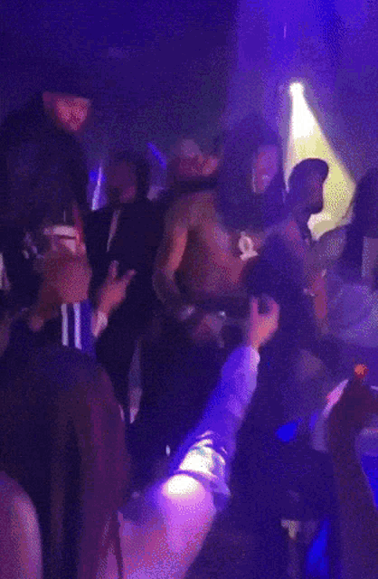 a crowd of people are dancing in a dark room with blue lights behind them