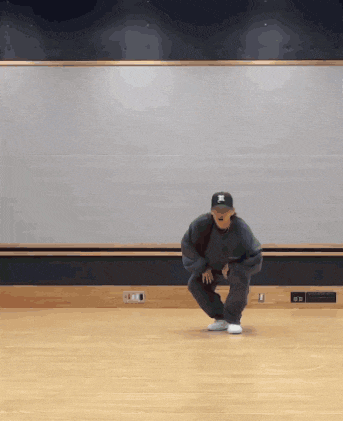 a man in a black hat is squatting on a wood floor