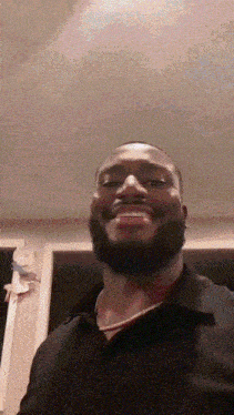 a man with a beard wearing a black shirt and a necklace smiles for the camera