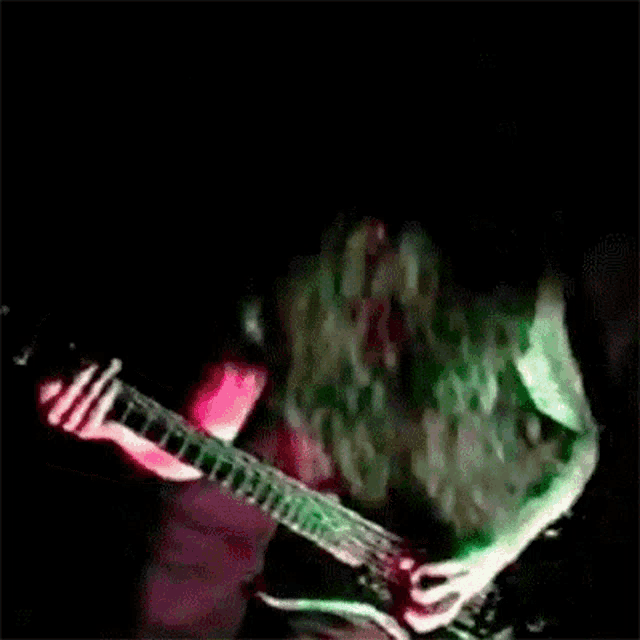 a man with green hair is playing a guitar in a dark room