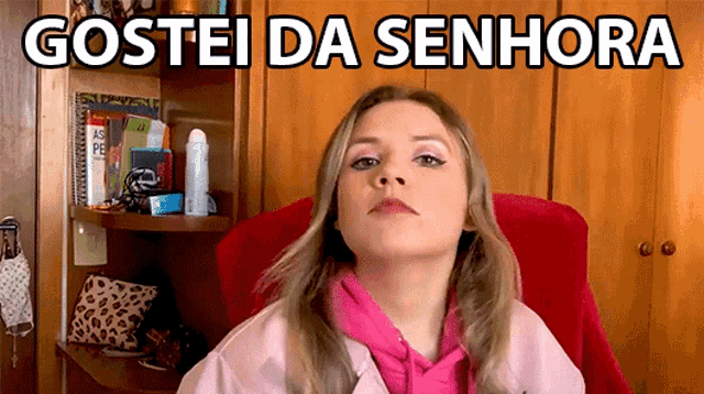 a woman in a pink jacket sits in a red chair with the words gostei da senhora above her head