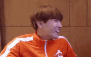a man in an orange jacket is laughing with his mouth wide open .
