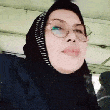 a woman wearing glasses and a hijab is looking at the camera