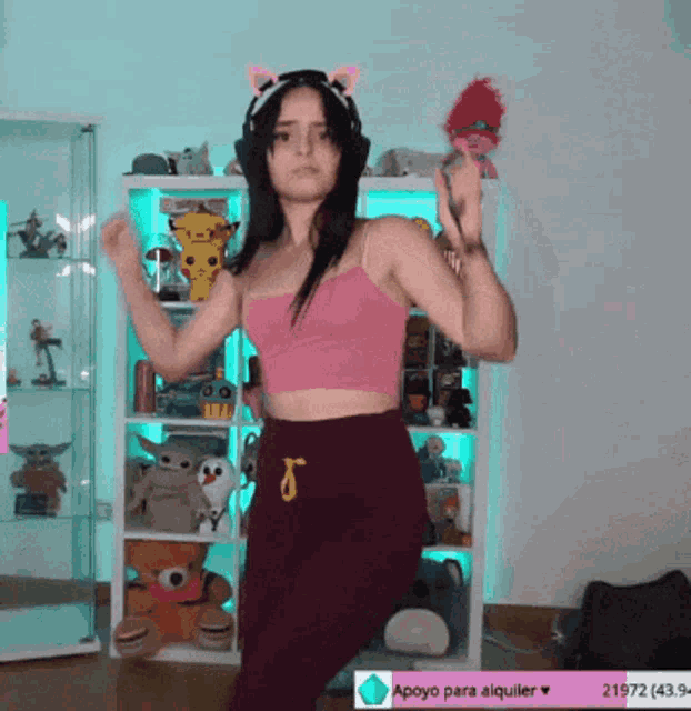a woman in a pink top and purple pants is dancing in front of a shelf filled with stuffed animals