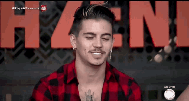 a man in a red and black plaid shirt is smiling in front of a large red hzen sign