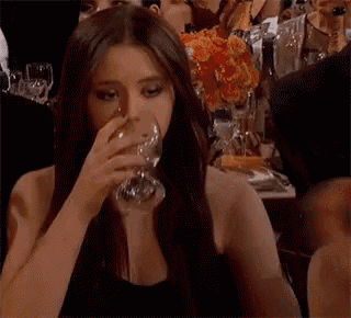 a woman is drinking a glass of wine in a crowded room .