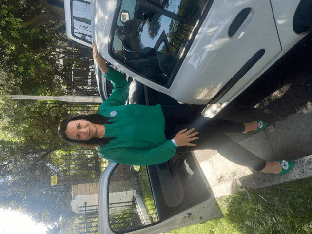 a woman in a green shirt stands next to a white car with the door open