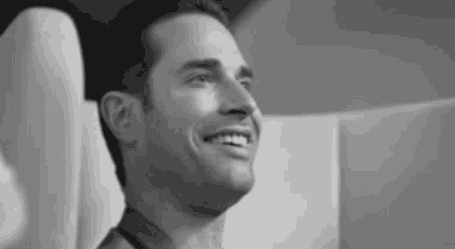 a black and white photo of a man smiling while sitting in a chair .