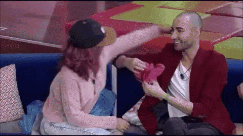 a man and a woman are sitting on a couch and the woman is putting her hand on the man 's head