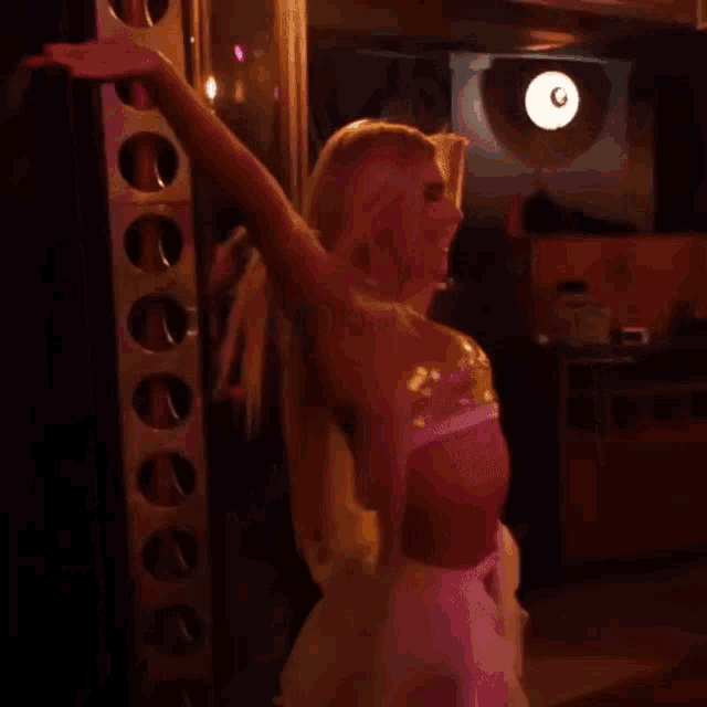 a woman in a white dress is standing in a dark room with a pink light behind her .