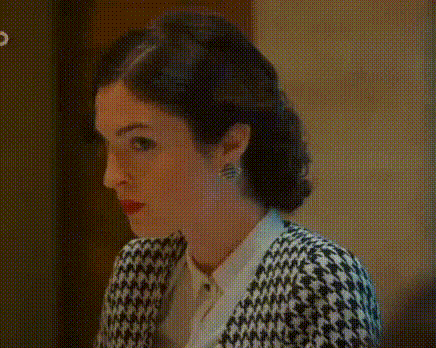 a woman wearing a black and white houndstooth sweater and a white shirt is looking at the camera .