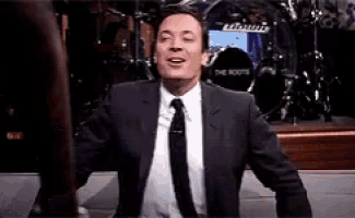 a man in a suit and tie is standing in front of a drum set and smiling .