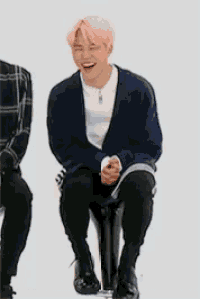 a young man with pink hair is sitting on a chair