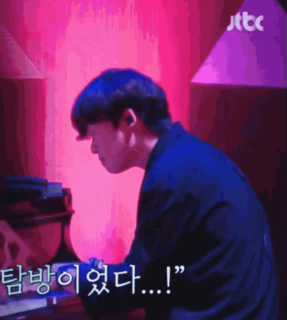 a man is sitting at a desk with a jtbc logo behind him