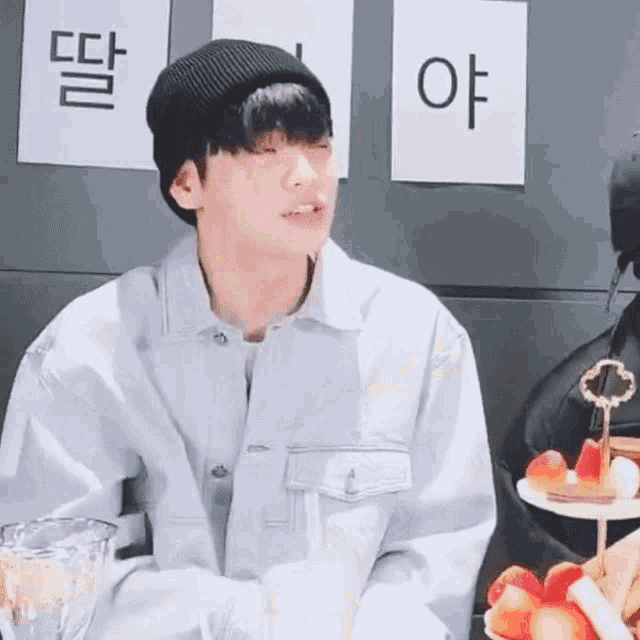 a young man wearing a beanie and a jacket is sitting at a table