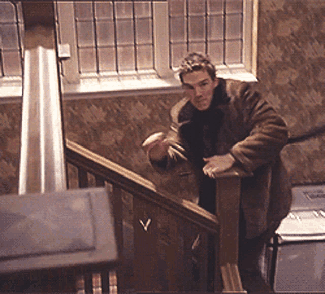 a man in a brown coat is standing on a set of wooden stairs