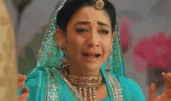 a woman in a blue dress is crying while wearing a gold necklace .