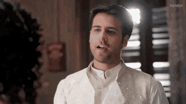 a man in a white vest is talking to a woman in a room with a hotstar logo in the corner