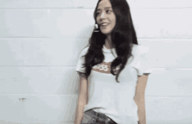 a woman wearing a white t-shirt and jeans is standing in front of a white brick wall .