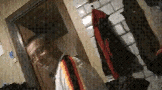 a man wearing glasses and a scarf stands in a hallway