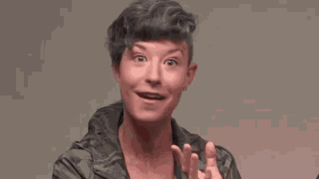 a woman with short gray hair is wearing a camouflage jacket and making a funny face .