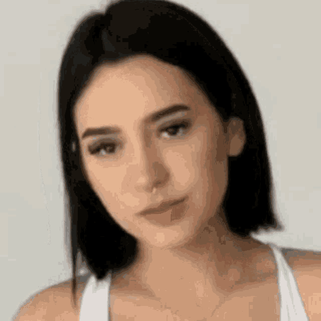 a woman with black hair and a nose ring is wearing a white tank top and a necklace .