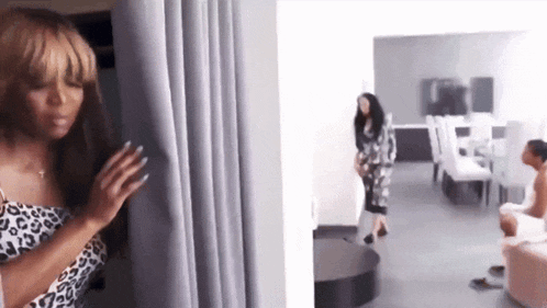 a woman in a leopard print dress is standing behind a curtain in a room .