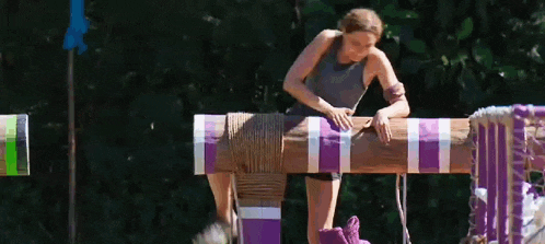 a woman is standing on a wooden post with purple stripes .
