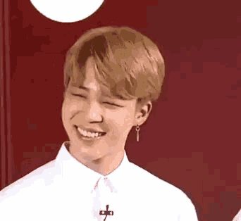 a young man wearing a white shirt and earrings is smiling and looking at the camera .