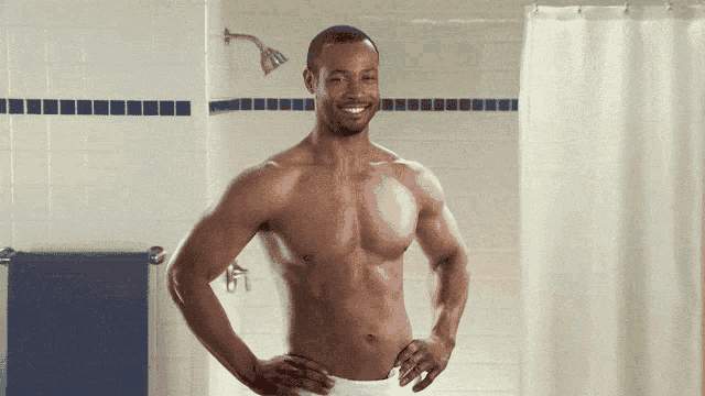 a shirtless man smiles in a bathroom with his hands on his hips