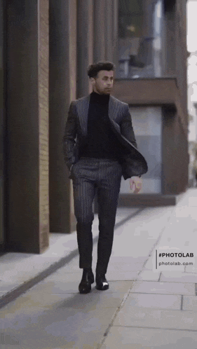 a man in a suit and black turtleneck is walking down the street .