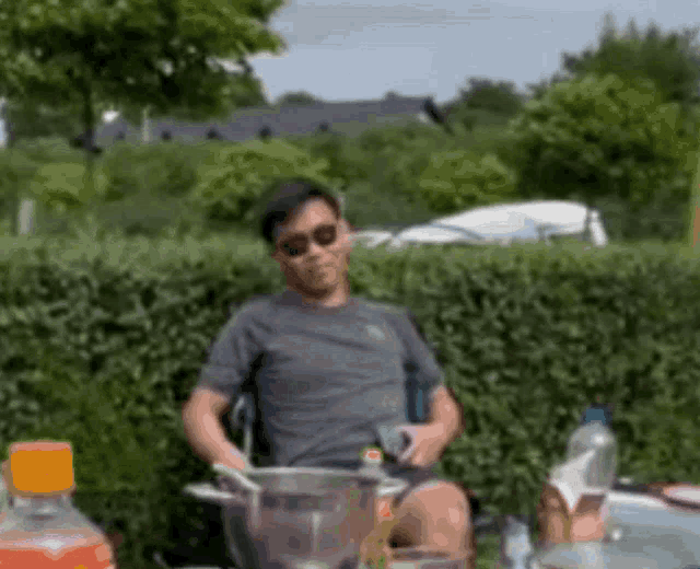 a man in sunglasses sits at a table with a bottle of orange soda in front of him