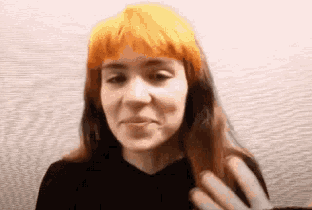 a woman with orange hair and a black shirt is smiling and looking at the camera .