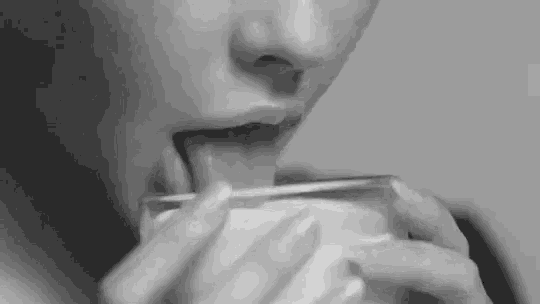 a black and white photo of a woman licking a glass .