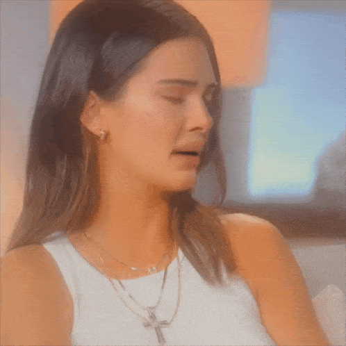 a woman wearing a white tank top and a necklace with a cross on it is crying .