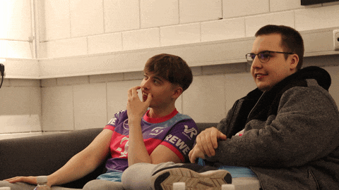 two young men sitting on a couch one wearing a rewe shirt