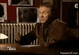 a man in a suit is sitting at a desk with his hands out .
