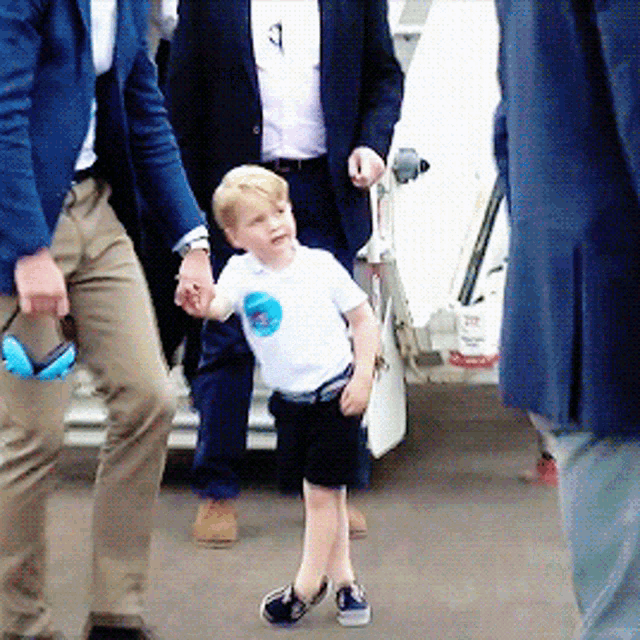 a little boy wearing a white shirt with a blue circle on it is walking between two men