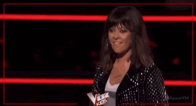 a woman in a black jacket is making a funny face while standing in front of a red wall .