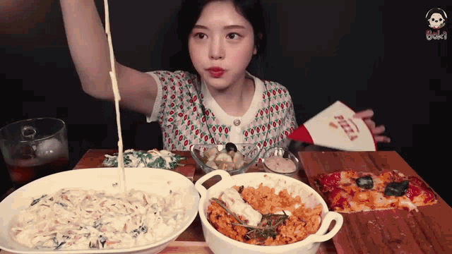 a woman is sitting at a table with plates of food and a cone that says pizza
