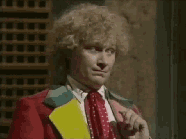 a man with curly hair is wearing a red suit and tie and holding a microphone .