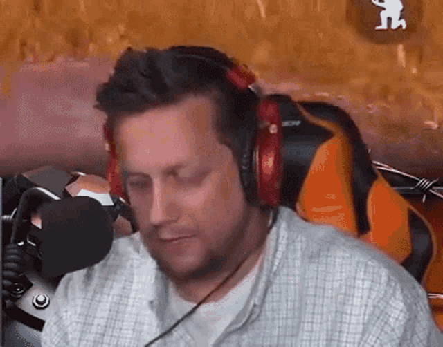 a man wearing headphones is sitting in front of a microphone in a gaming chair .