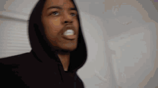 a man in a black hoodie is making a funny face while standing in a room .