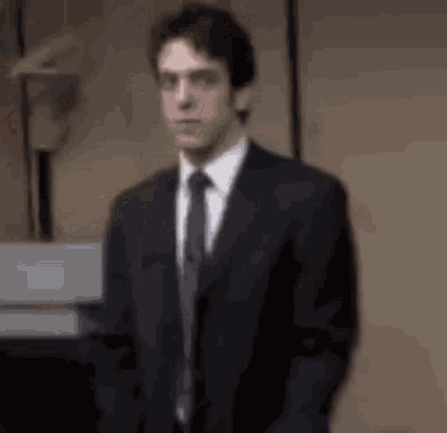 a man in a suit and tie is standing in a room in front of a wall .