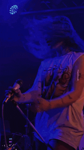 a woman with blue hair is singing into a microphone while wearing a t-shirt that says ' nirvana '