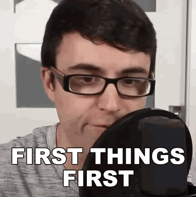 a man wearing glasses says first things first in front of a microphone .